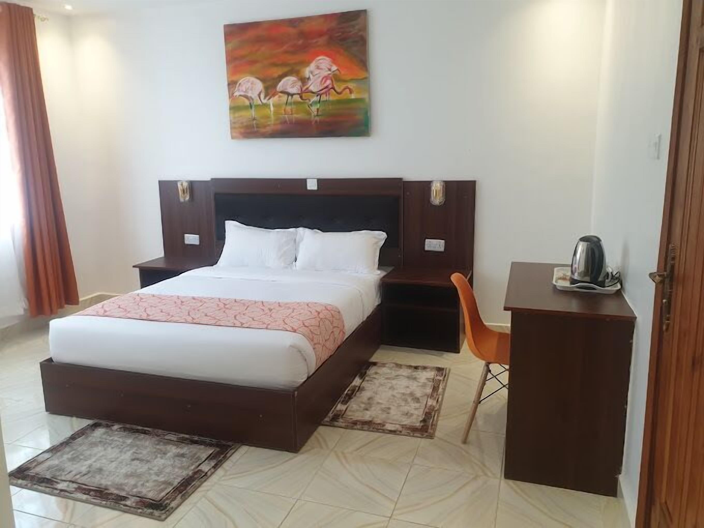 Habitación de hotel con una cama grande, un escritorio con silla, un cuadro en la pared y una cafetera sobre el escritorio.