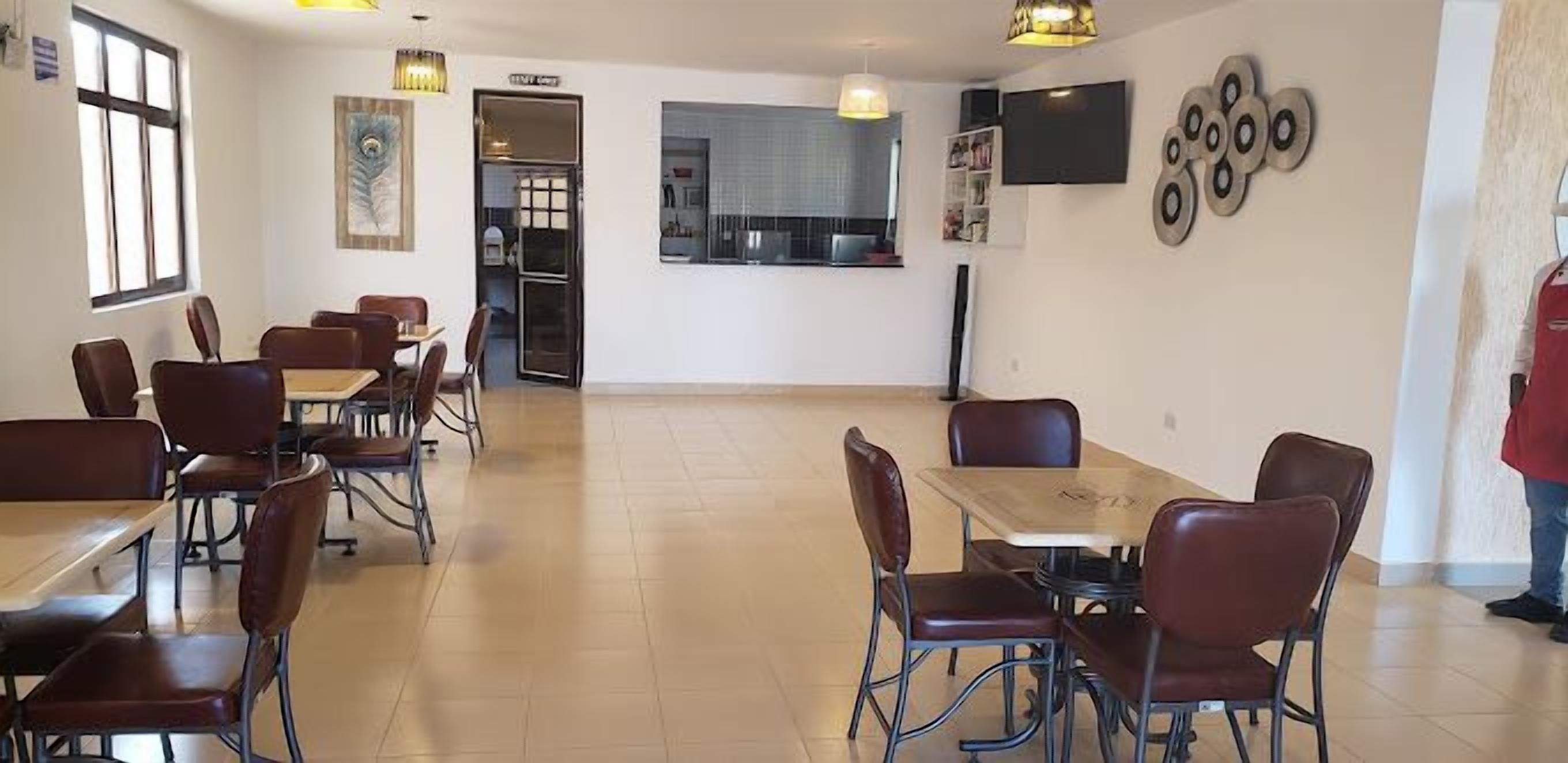 Un comedor con mesas y sillas, una cocina al fondo y una persona de pie cerca de la puerta.