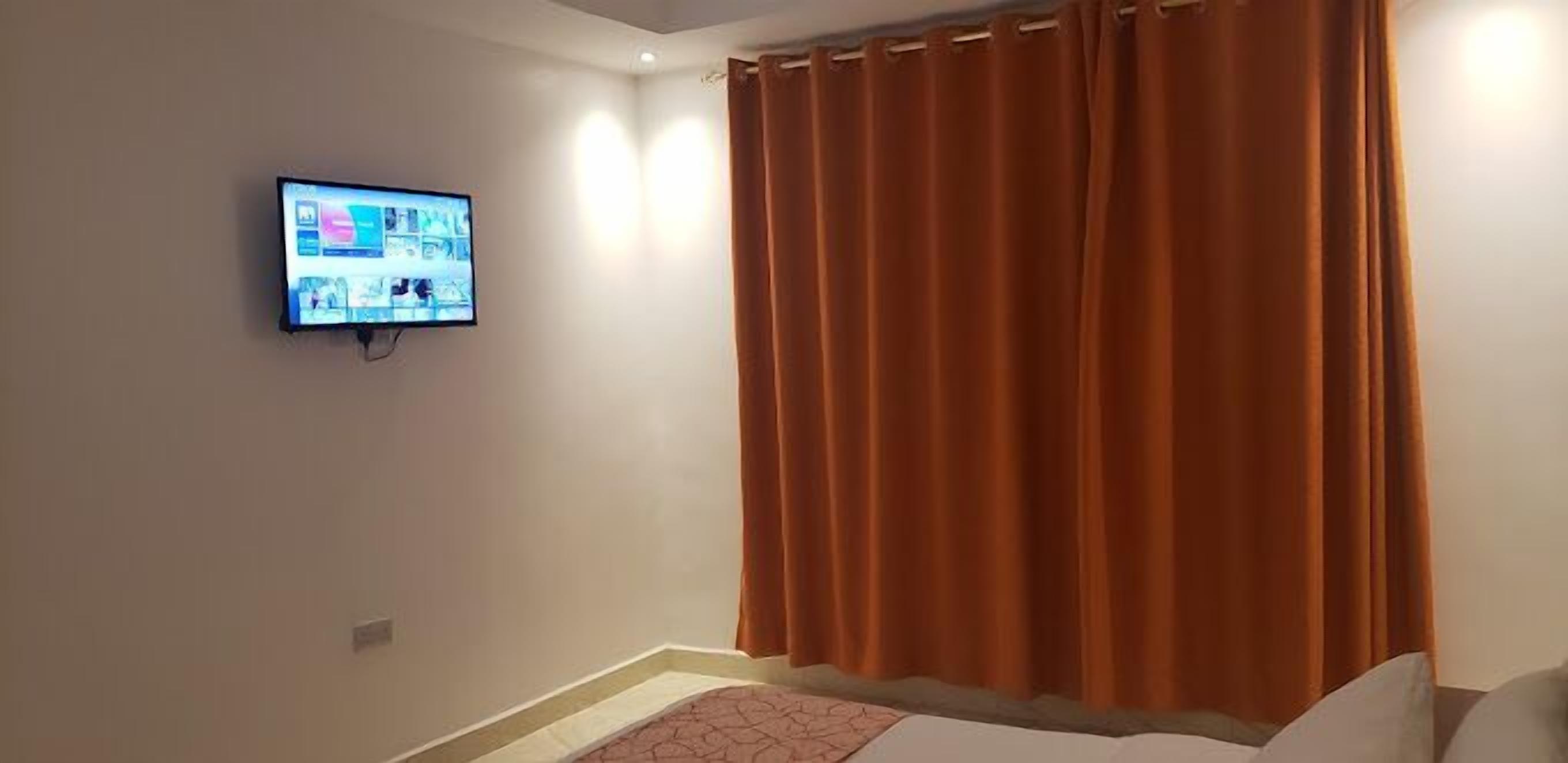Una habitación de hotel con cama, televisión montada en la pared y ventana con cortinas.
