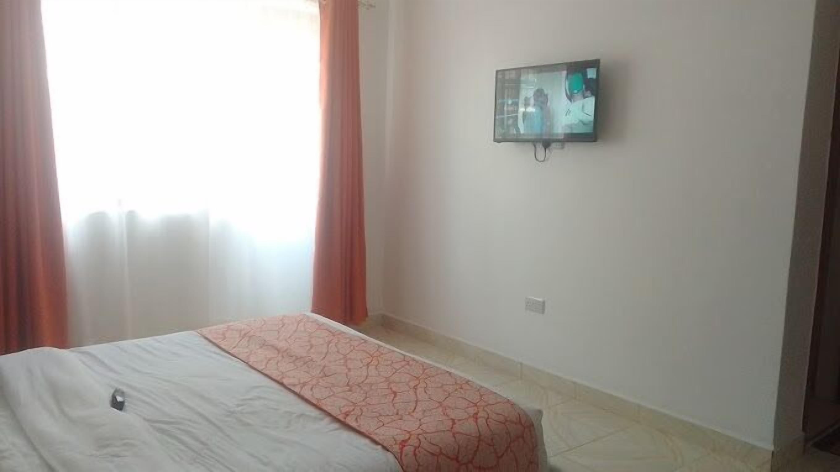 Habitació d'hotel amb un llit, un televisor fixat a la paret i una finestra amb cortines.
