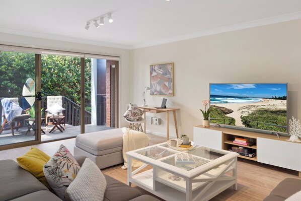A modern living room with a large TV, comfortable seating, and a view of the outdoors.