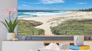 Une vue sur la plage depuis un balcon, avec un plateau contenant divers objets, notamment un livre, une tasse et un bol décoratif.