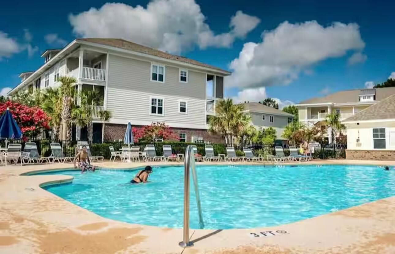 Zona de piscina con sillones de descanso y un edificio con balcones.