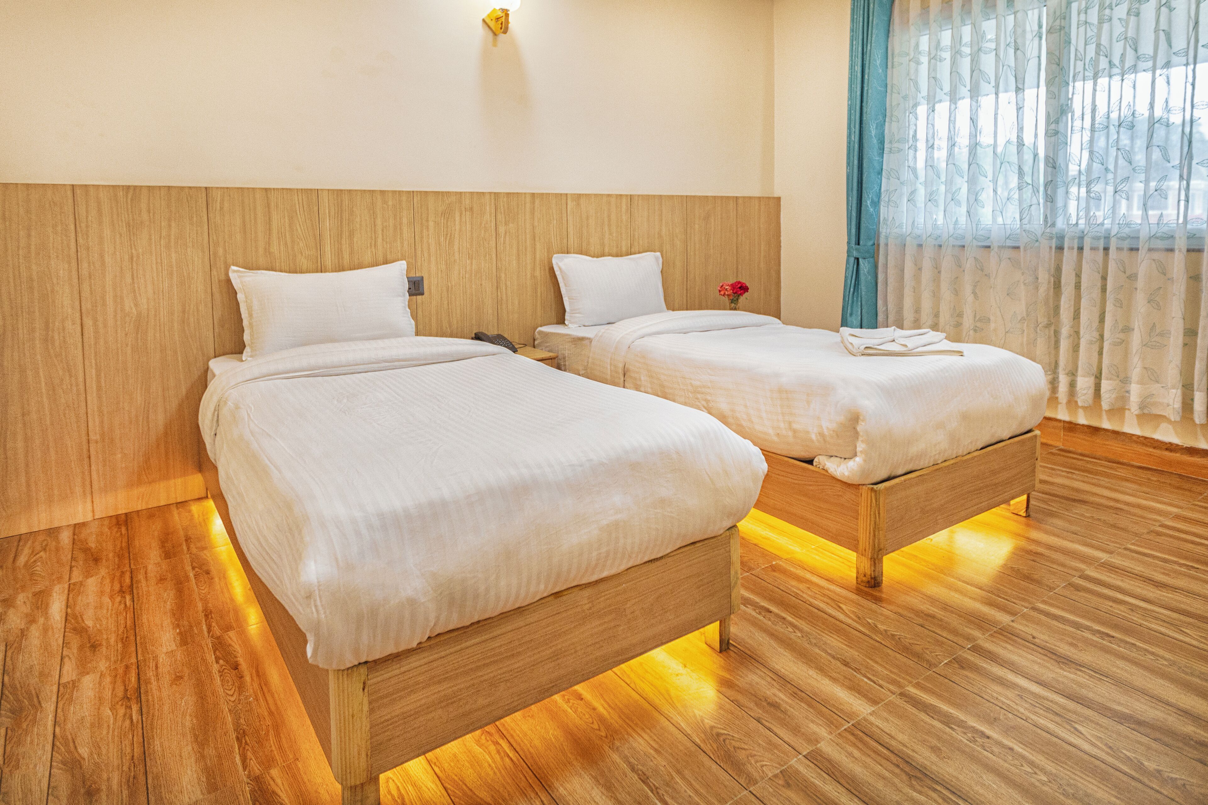 Habitación de hotel con dos camas de madera, cabeceros de madera y un ventanal con cortinas traslúcidas.