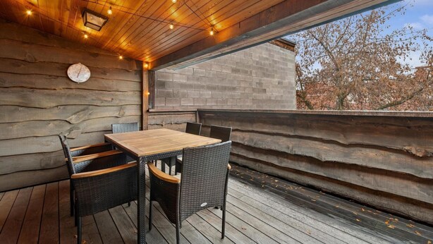 A wooden deck with a table and chairs, a clock on the wall, and a view of trees and a building through a window. - Walk to Shopping | 15 Mins to the Resort (Whitefish)