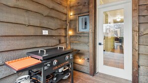 A wooden interior with a grill station and a door leading to a room. - Walk to Shopping | 15 Mins to the Resort (Whitefish)