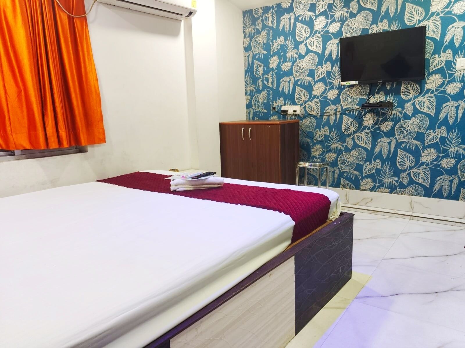 A bedroom with a bed, a wardrobe, a television mounted on the wall, and a window with curtains.