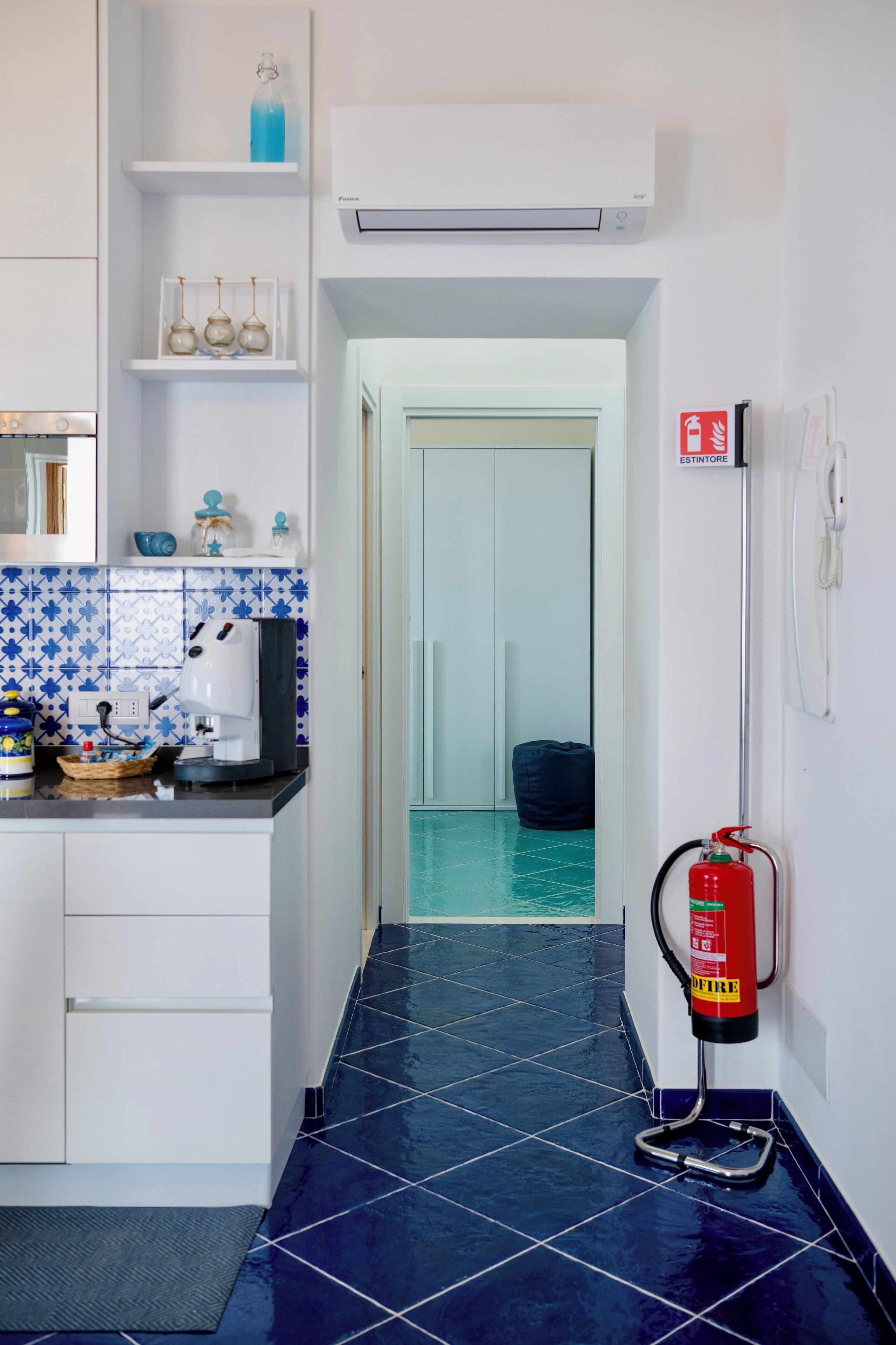 A kitchen with white cabinets, a coffee machine, and a blue tiled backsplash.