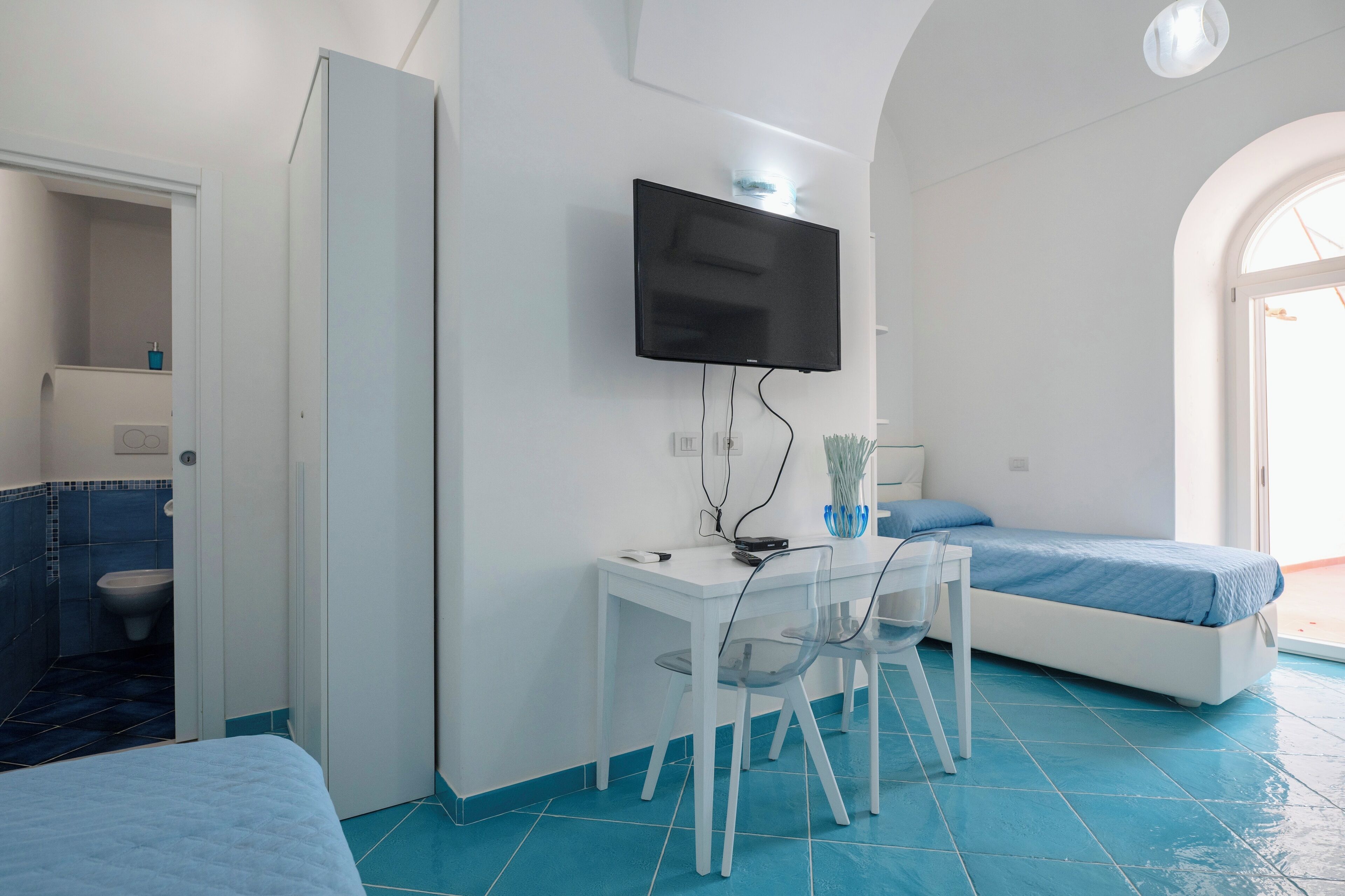 Ein Zimmer mit Bett, Schreibtisch mit Stuhl, Fernseher an der Wand und einem Badezimmer mit Toilette und Waschbecken.
