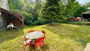 Een achtertuin met een houten tafel en rode stoelen, omringd door gras en bomen.