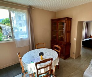 A dining area with a round table, chairs, a cabinet, and a window with curtains. - Le Flocon Le Mont Dore 4 pers (Mont-Dore)