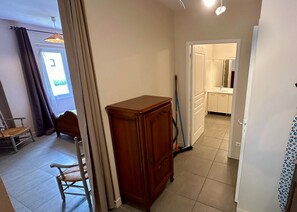 A room with a wooden cabinet, a chair, a broom, and a door leading to a bathroom. - Le Flocon Le Mont Dore 4 pers (Mont-Dore)