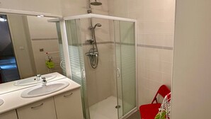 Een badkamer met een douchecabine van glas, een wastafel met spiegel en een rode stoel.
