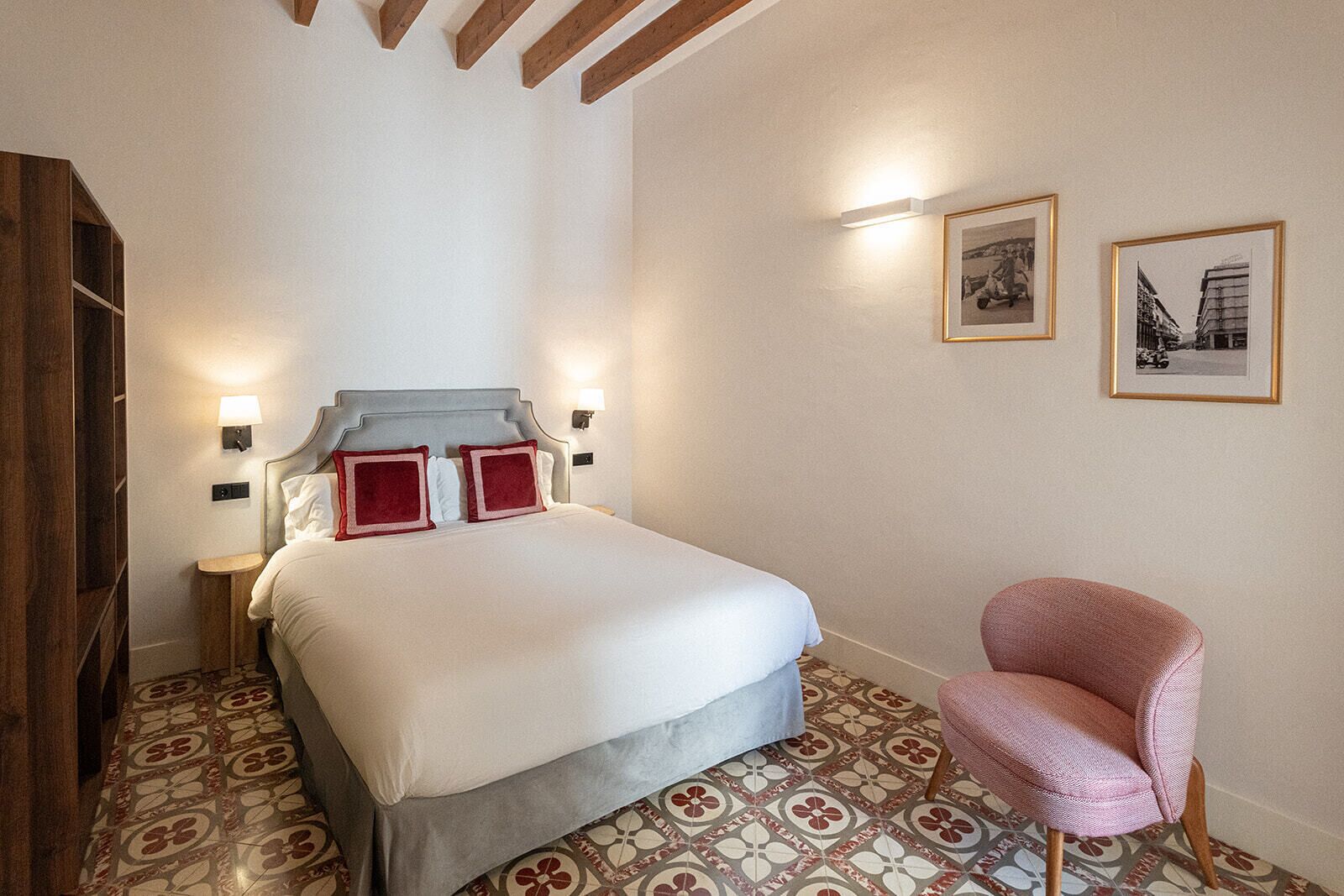 Un dormitorio con una cama, una silla, una mesita de noche y dos lámparas de pared.