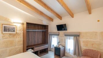 Habitación con vigas de madera a la vista, un armario de madera, un televisor, una mesita con una tetera y una silla estampada.