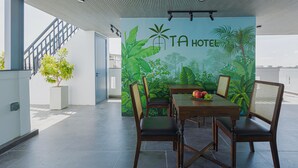 A modern outdoor dining area with a mural of tropical plants and the text "TA HOTEL" on the wall.