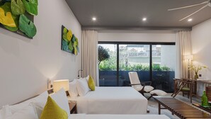 A hotel room with two beds, a desk, a chair, and a view of greenery outside.