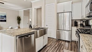 Una cocina moderna con electrodomésticos de acero inoxidable, armarios blancos y encimera de granito.
