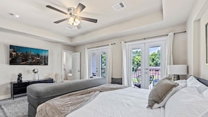 Un dormitorio con cama, un banco, un ventilador de techo y un cuadro de un paisaje urbano.