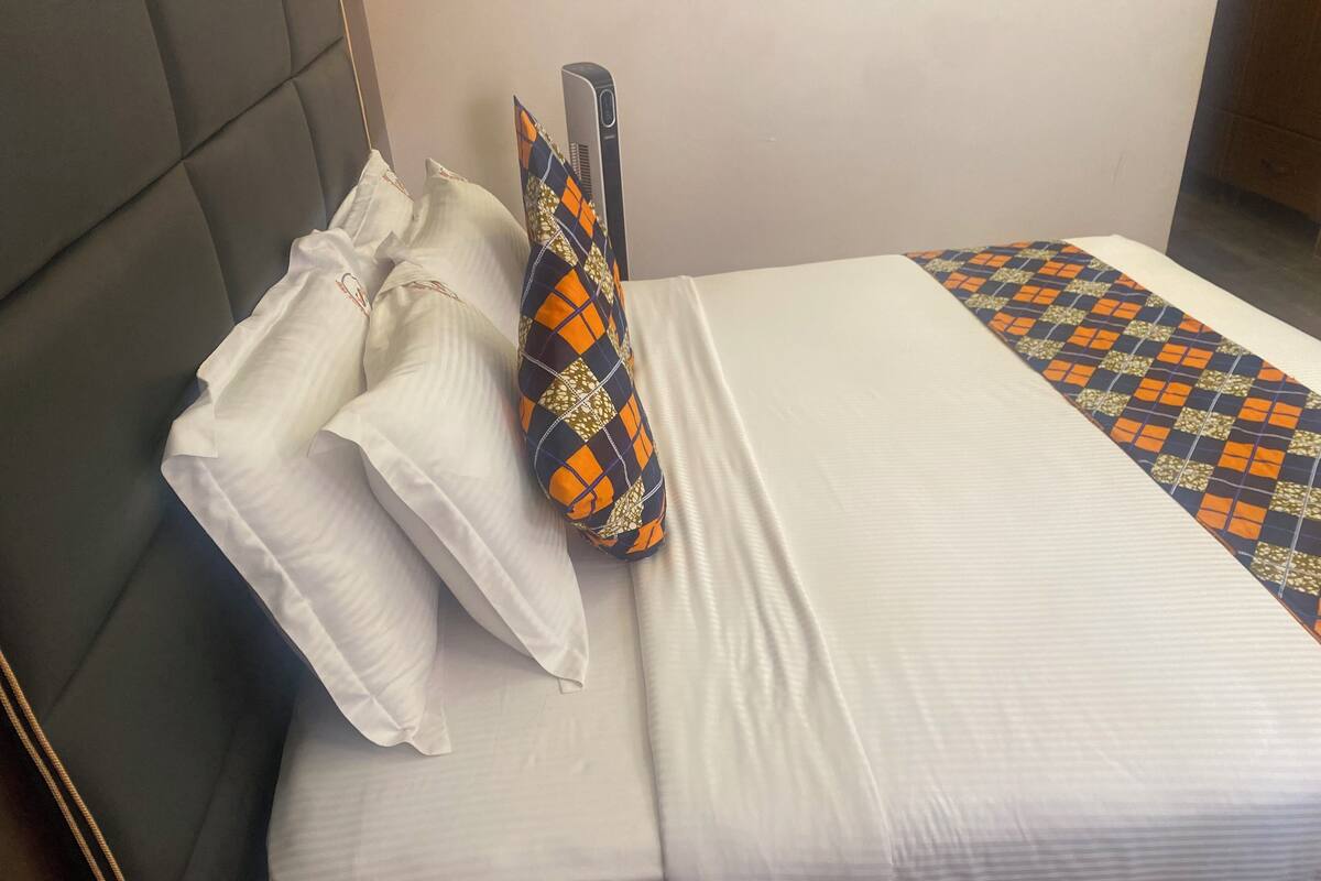 A neatly made bed with white linens, a patterned blanket, and a decorative pillow.
