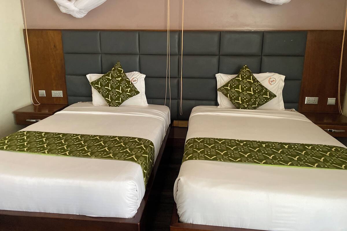 A hotel room with two beds, each with a green patterned bedspread and matching pillows.