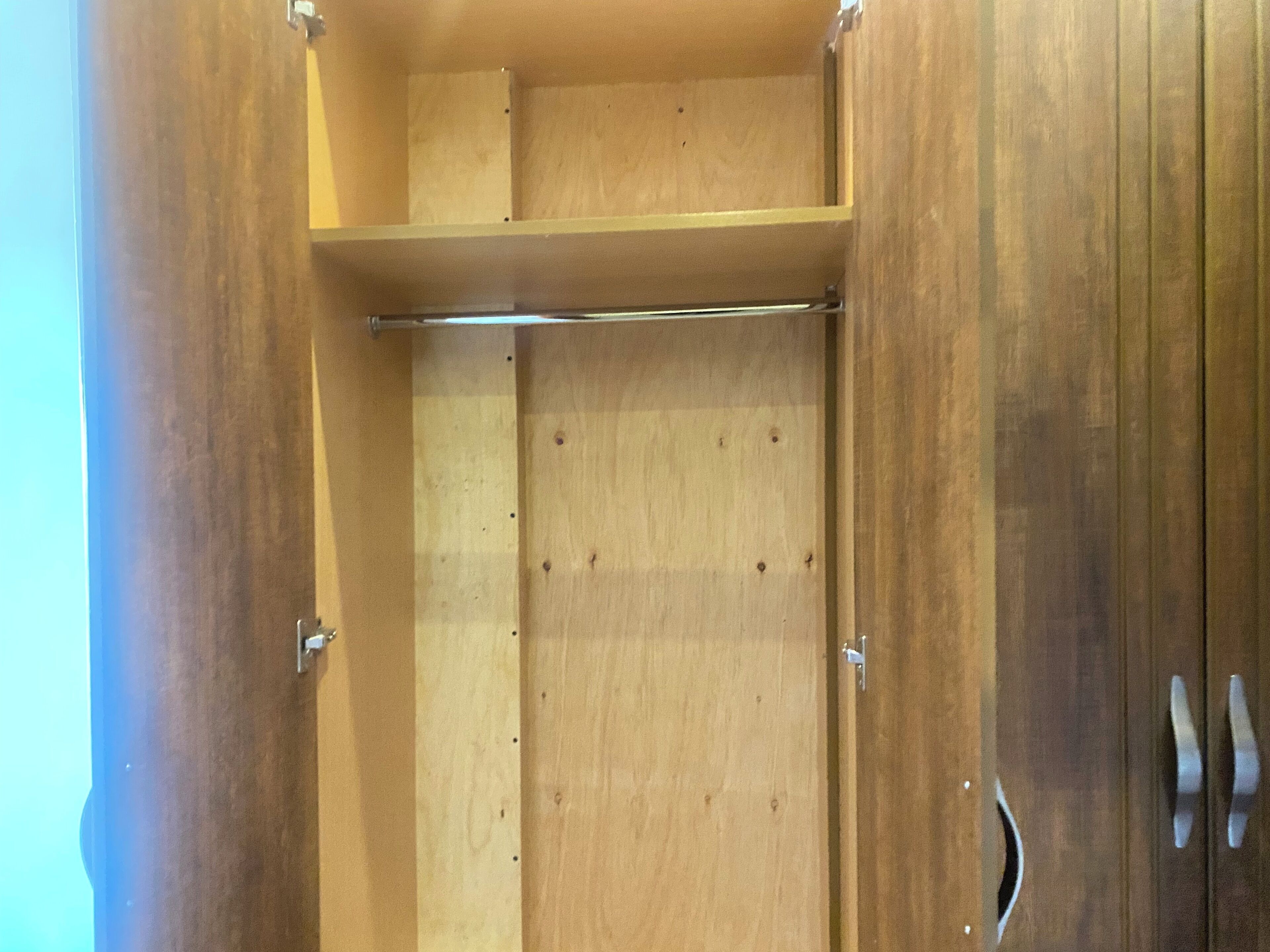 A wooden wardrobe with a hanging rod and a shelf.