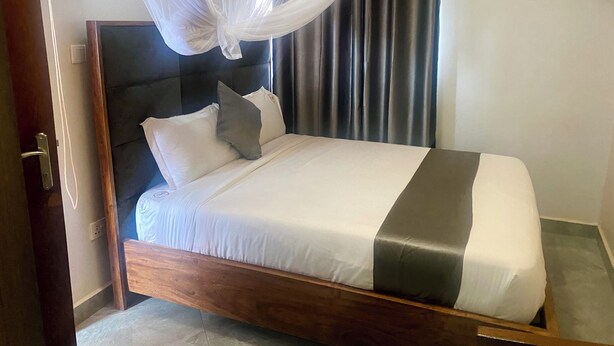 A neatly made bed with a wooden frame, white and gray bedding, and a canopy. - Jinna suites limited (Seeta)