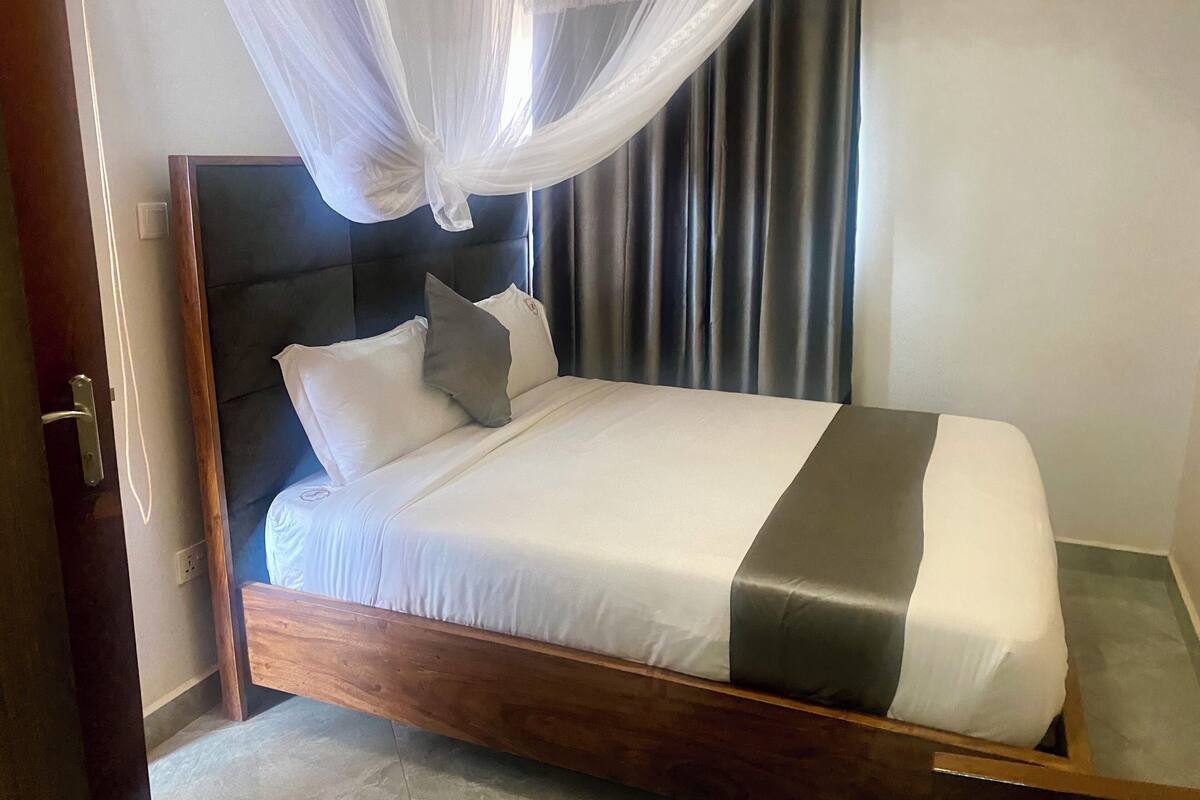 A neatly made bed with a wooden frame, white and gray bedding, and a canopy.