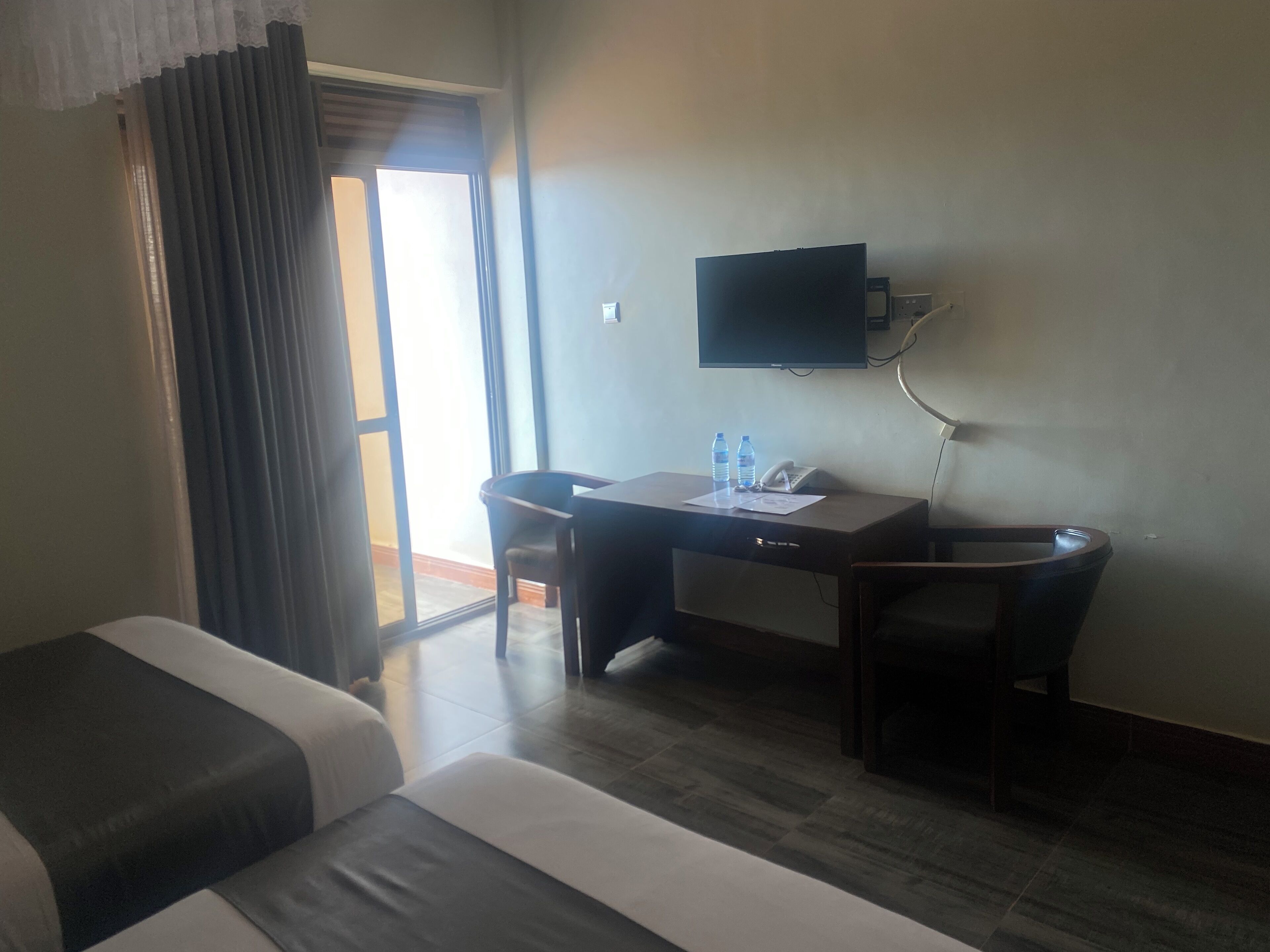 A hotel room with a bed, a desk with a chair, a television, and a window with curtains.