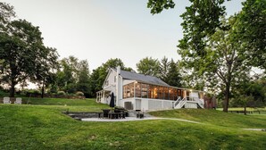 Ein weißes Haus mit einem großen Fenster, einer Veranda und einem kleinen Teich im Vorgarten.