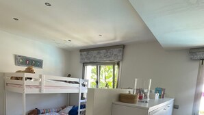 Une chambre avec deux lits superposés, un petit bureau, un tapis rayé aux couleurs vives et une fenêtre donnant sur un paysage verdoyant.