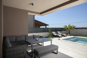 A modern outdoor living area with a pool, seating, and a covered patio.