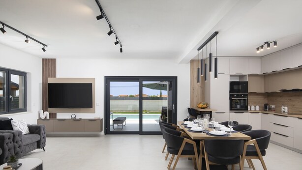 A modern living room with a flat-screen TV, a sofa, and a dining area with a table set for four. - Villa del Sol near Fažana (Valbandon)
