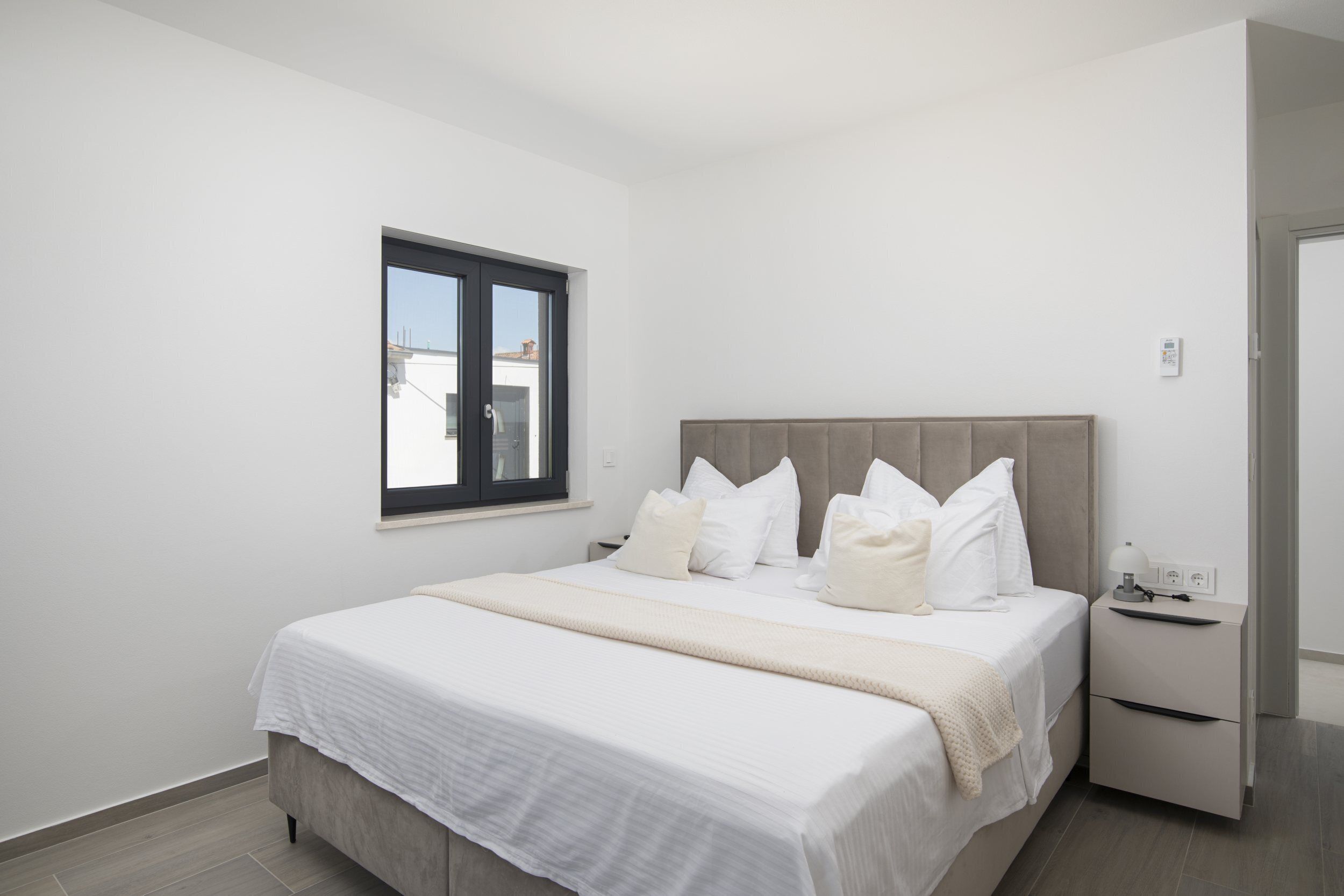 A bedroom with a bed, a nightstand, a window, and a door.