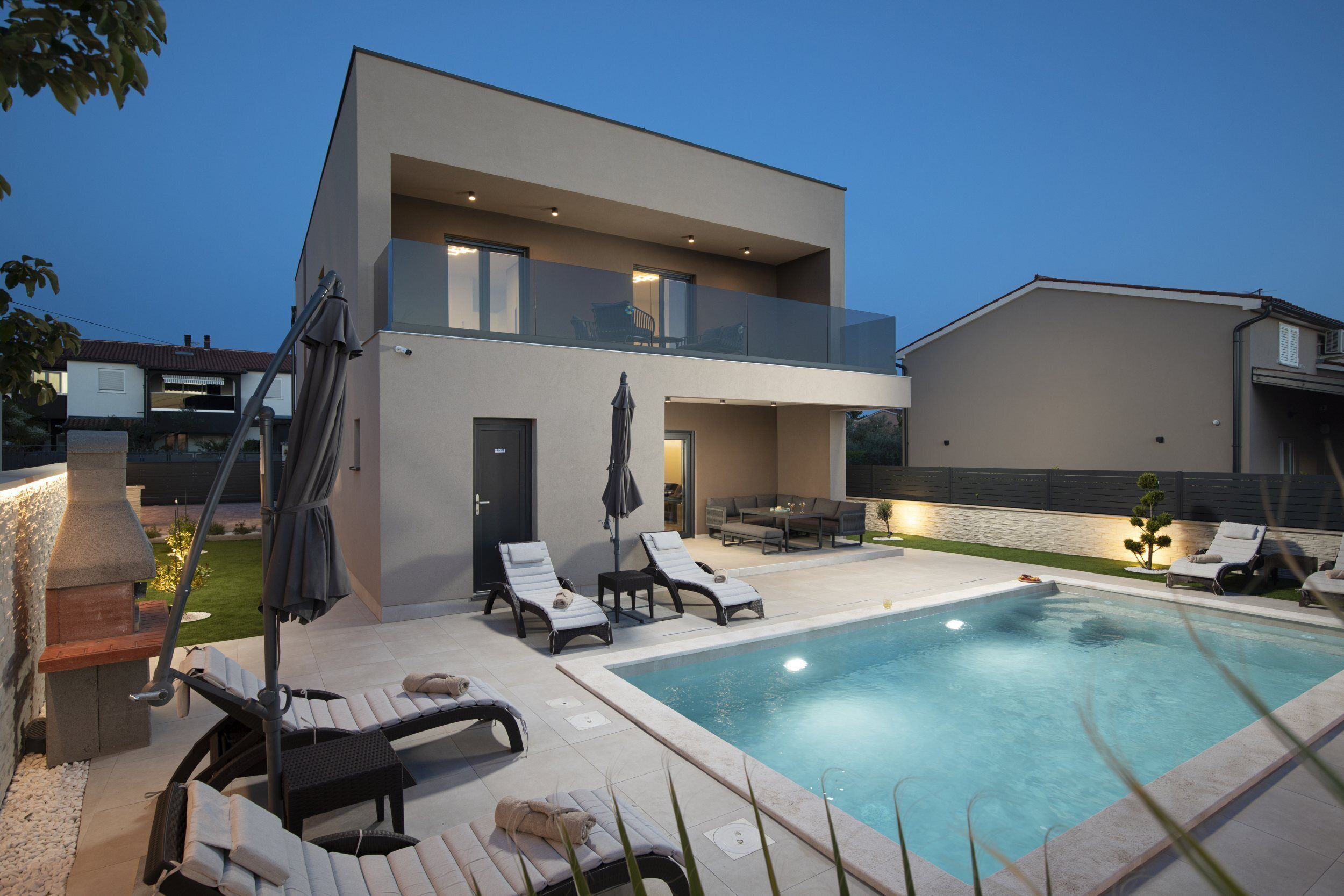 Une maison moderne à deux étages dotée d’une piscine, d’un espace salon extérieur et d’un coin barbecue.