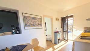 A modern kitchen with a built-in oven and a sink, a dining area with a table and chairs, and a private terrace accessible through a door. - Dammuso - Cala Cinque Denti - AFFITTI\'CA (Pantelleria)