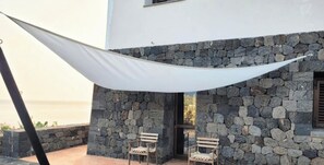 A stone building with a white awning, two wooden chairs, and a view of the sea. - Dammuso - Cala Cinque Denti - AFFITTI\'CA (Pantelleria)
