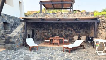 Eine private Terrasse mit Steinboden, einem Grillbereich und Gartenmöbeln.
