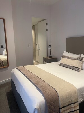 A neatly made bed with a quilted blanket, a bedside lamp, and a nightstand. - The Rubik Executive Apartment (Cape Town)