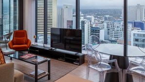 Una sala de estar moderna con un televisor grande, una mesa de centro de vidrio, un sofá y una mesa de comedor con sillas.