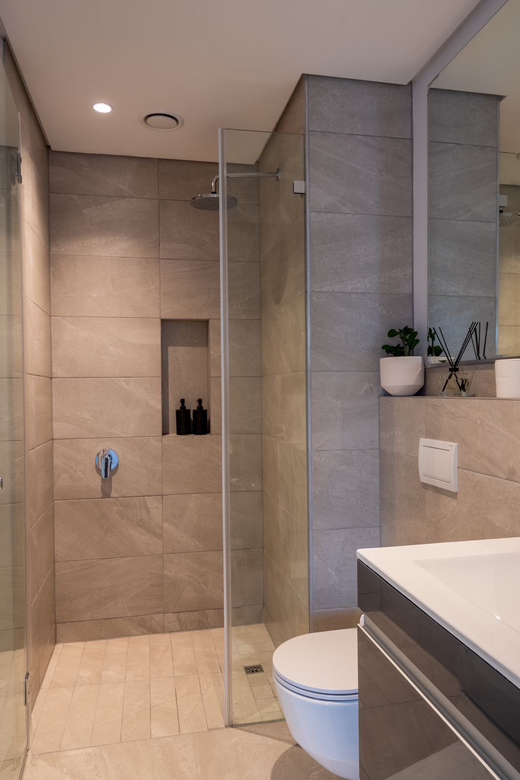 A modern bathroom with a glass-enclosed shower, a toilet, and a vanity with a mirror.