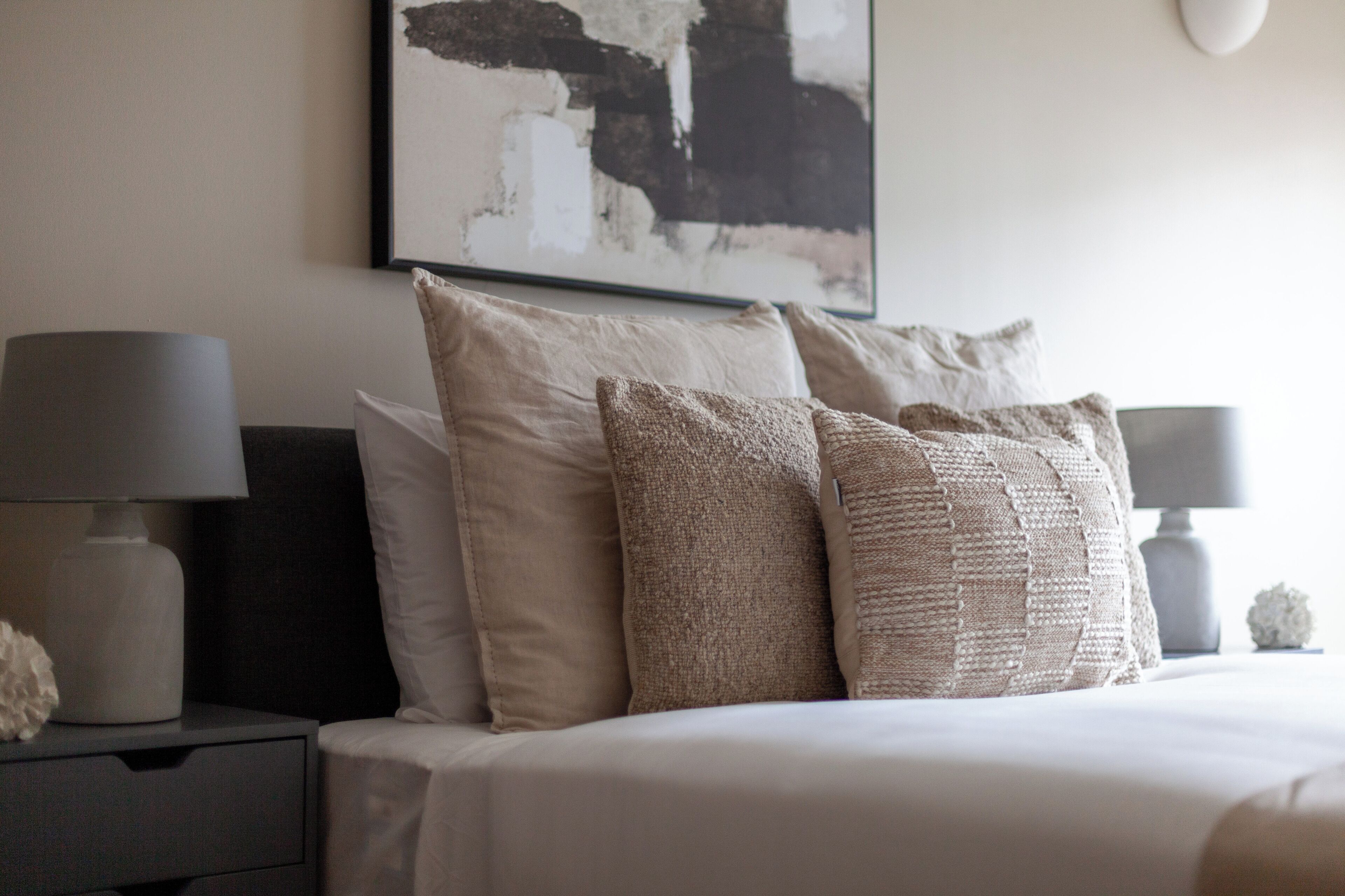 A neatly made bed with multiple pillows and a bedside table with a lamp.