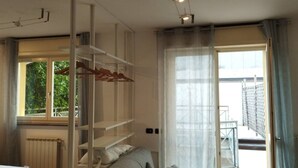 A bedroom with a bed, a wardrobe, a radiator, a window with a view of greenery, and a door leading to an outdoor area. - Liguria 51 - RENT'CA (Milano)
