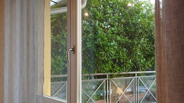 A window with a metal railing and a view of a green hedge outside. - Liguria 51 - RENT'CA (Milano)