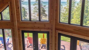A cabin with multiple large windows offering ocean views, deck seating, and a wooden interior.
