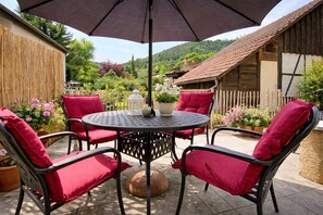 A round metal table with four chairs, each with a red cushion, under a large umbrella. - Bollenhut 1 Time out in the countryside! FEELING GOOD. RELAX. ARRIVAL. (Unknown)