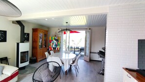 A modern living room with a white sofa, a dining table with chairs, a wooden cabinet, and a fireplace. - Peaceful house and wooded garden (Pornichet)