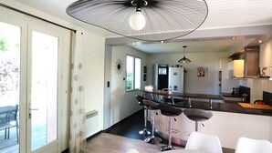 A modern kitchen with a bar area, a refrigerator, and a dining table with chairs. - Peaceful house and wooded garden (Pornichet)