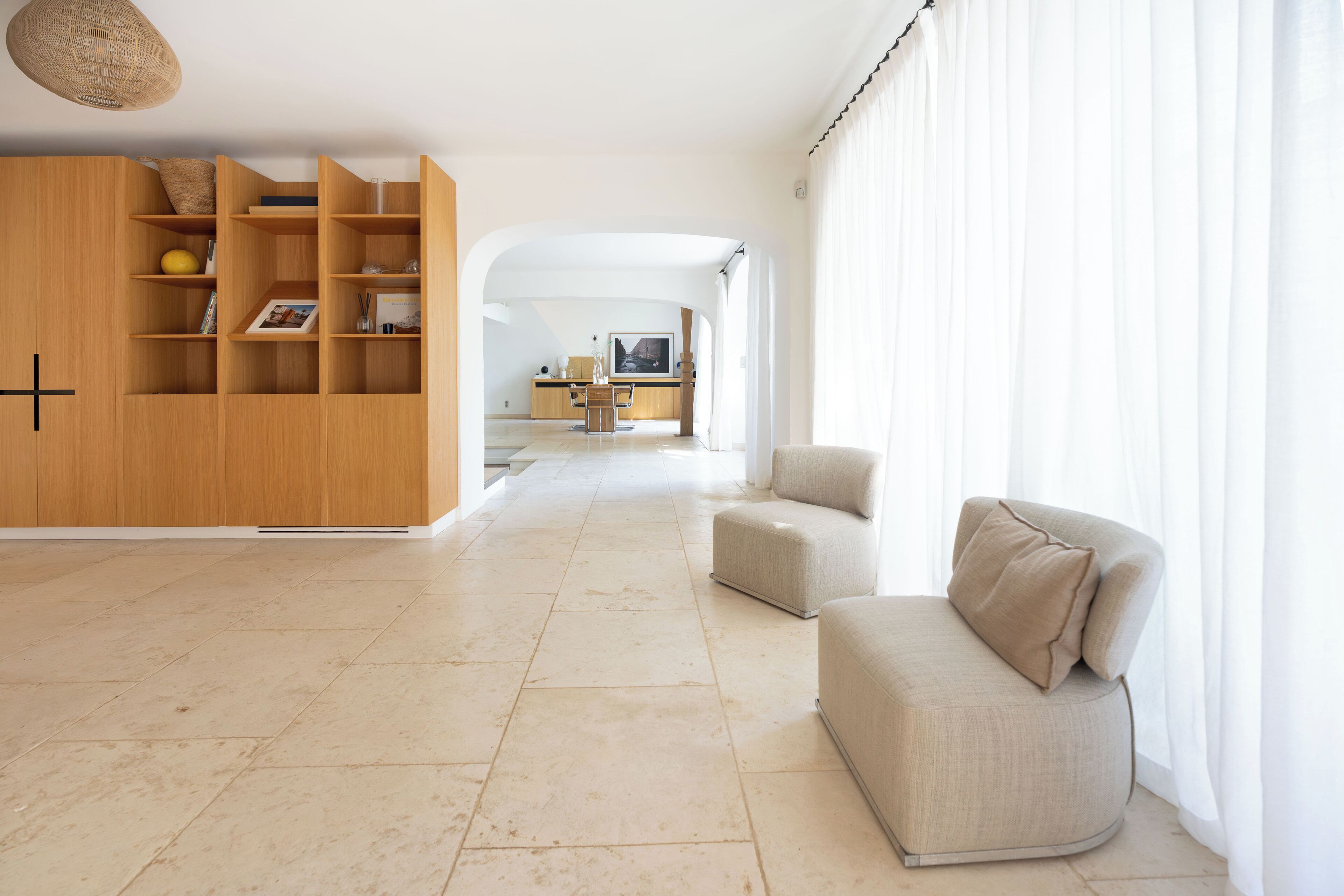 A spacious living area with a wooden cabinet, a beige sofa, and a kitchen in the background.