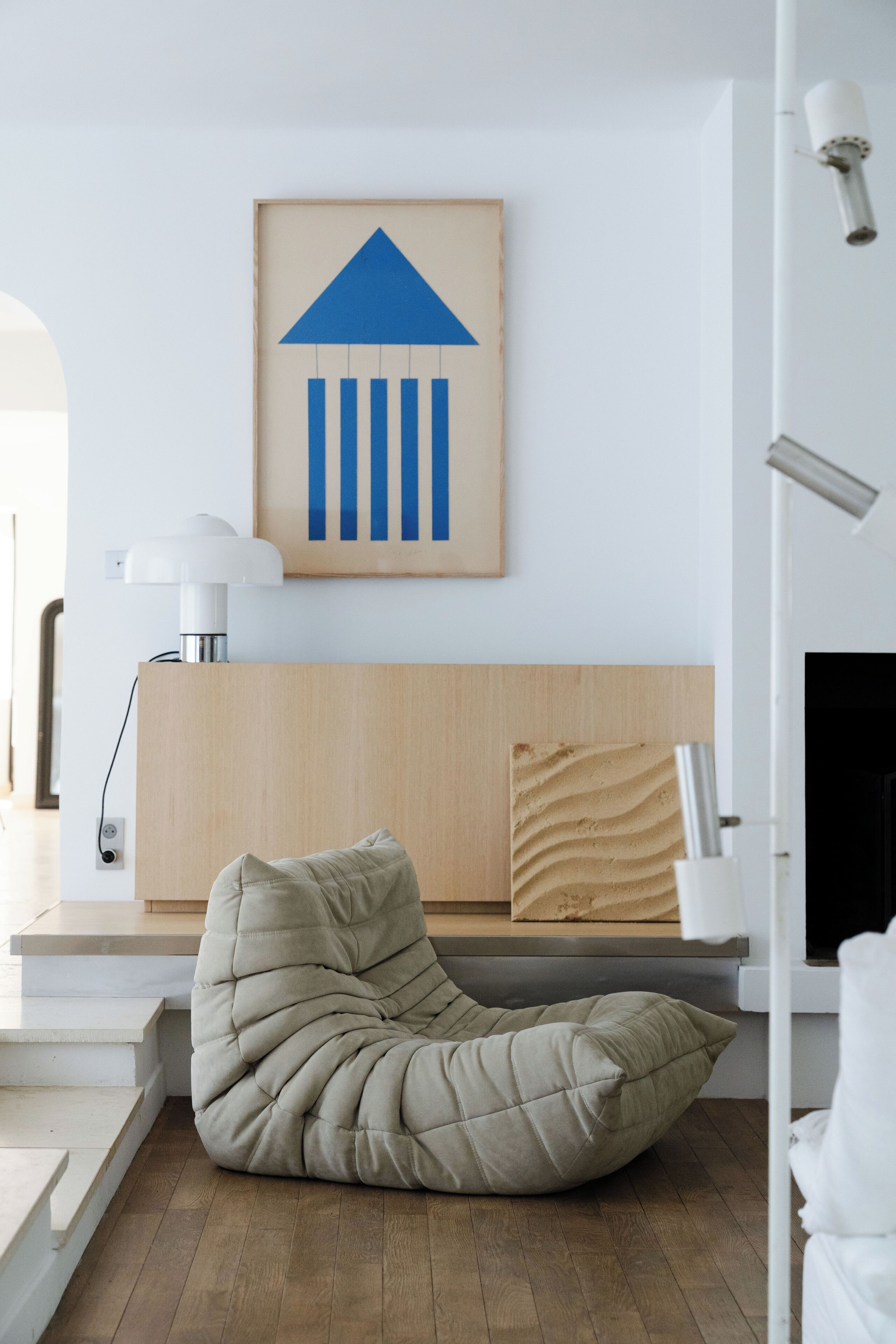 A modern living room with a beige bean bag chair, a wooden headboard, and a framed abstract artwork on the wall.